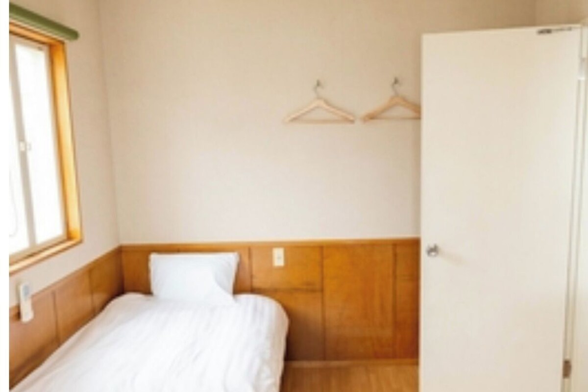 A hotel room with two beds, wooden flooring, a white door, and a window with blinds.