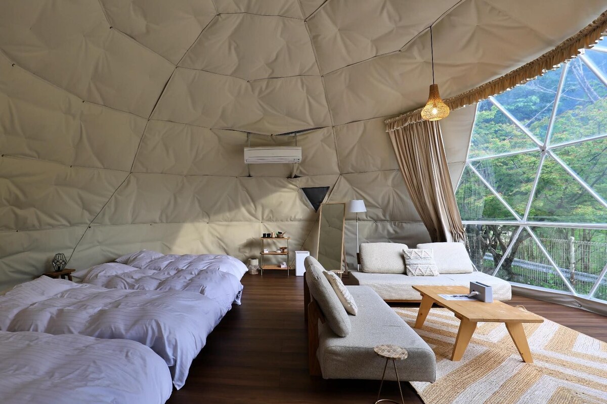 A spacious tent with two beds, a sofa, a table, and a lamp.