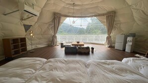 Een ruime tent met een groot bed, een klein tafeltje en een kast.