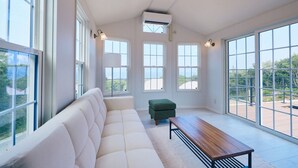A spacious room with a white sofa, a green ottoman, and a wooden bench. There are large windows providing a view of the outdoors. - Glamping Kashima 753 (Kashima)
