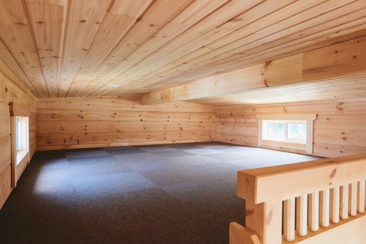 A wooden cabin interior with a high ceiling, a carpeted floor, and a small window.