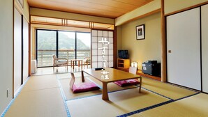 A traditional Japanese room with tatami flooring, a low table, and a sliding door leading to a balcony with a view of mountains. - Yasuragiso (Amakusa)