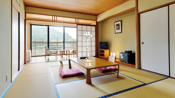 Una habitación japonesa tradicional con suelo de tatami, una mesa baja y una puerta corredera que da a un balcón con vistas a las montañas.