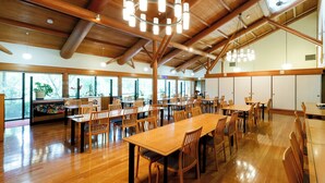 A spacious dining area with wooden tables and chairs, large windows, and a high ceiling with exposed beams. - Yasuragiso (Amakusa)