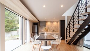 Un espace repas moderne avec une grande table, des chaises blanches et un vase de fleurs.