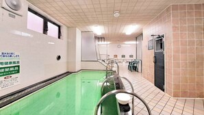 A public bath area with a green pool, tiled walls, and a clock on the wall. - Capsule Hotel Sauna Sun (Sasebo)