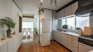 A modern kitchen with a refrigerator, microwave, sink, and stove. There are wooden cabinets, a dining area with a table and chairs, and a potted plant. - SEA Eirene Hillstop Onna-son (Onna)