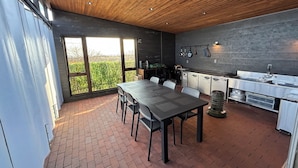 A modern kitchen with a large dining table, a built-in oven, and a view of greenery outside. - Villa Cortile (Awaji)