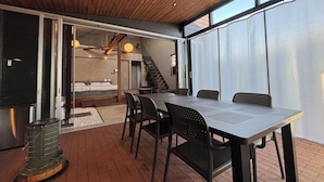 A modern outdoor dining area with a table and chairs, a staircase leading to an upper level, and a view of a bedroom with a bed and a staircase. - Villa Cortile (Awaji)