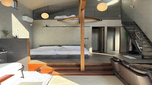 A modern loft bedroom with a large bed, a staircase, and a view of the city. - Villa Cortile (Awaji)