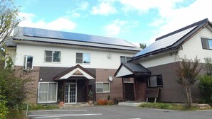 A building with a solar panel roof, a sign reading "YUZAN," and a parking lot. - Pension Yuuzann (Nagano)