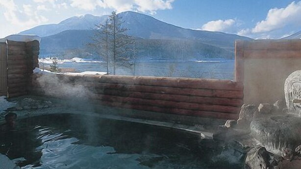 A rustic cabin with a wooden interior, a stone wall, and a view of a mountain and lake. - Pension Yuuzann (Nagano)