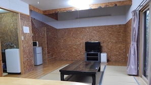 A room with a wooden floor, a television on a stand, a small refrigerator, and a water dispenser. - Pension Yuuzann (Nagano)