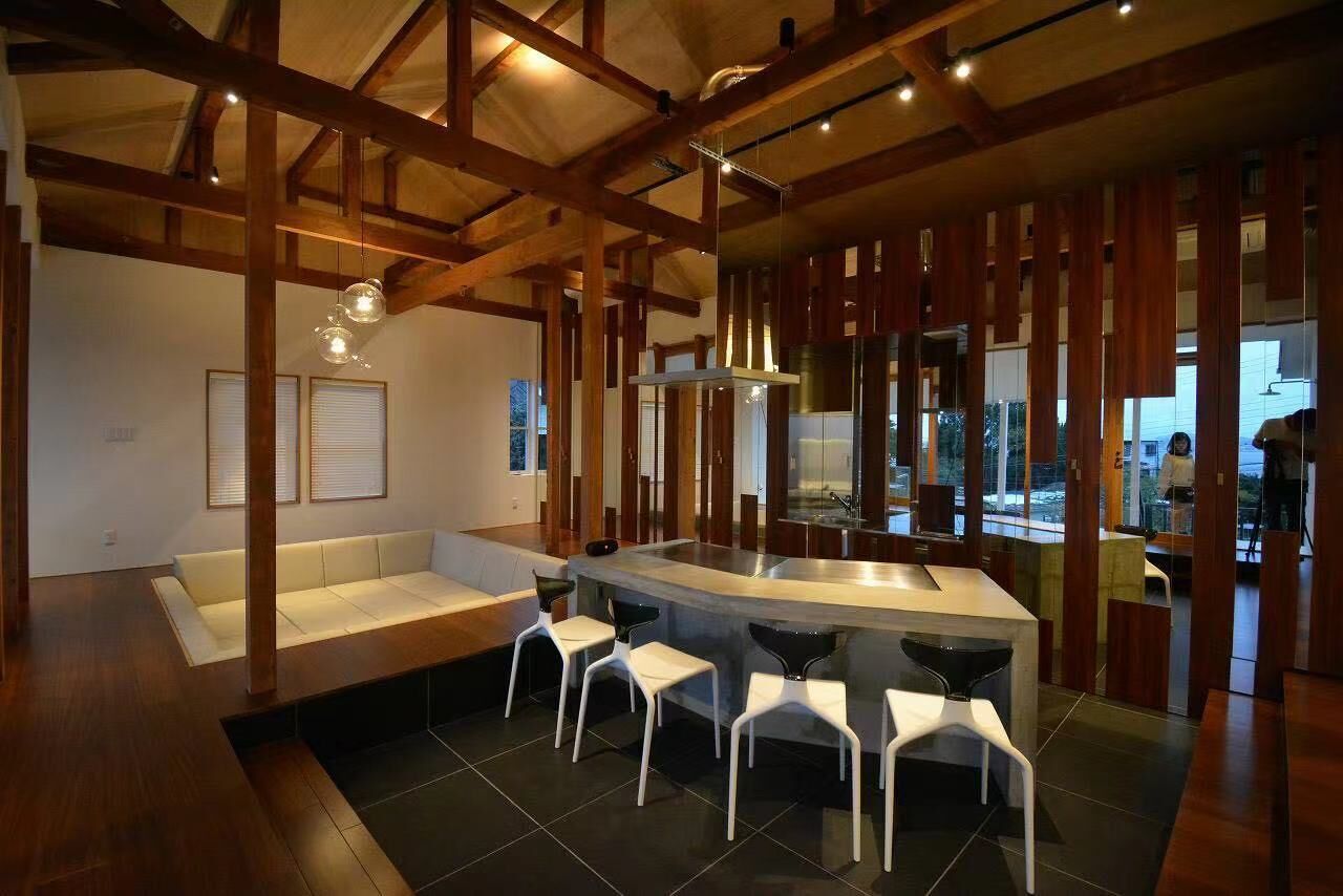 A modern kitchen with a central island, white bar stools, and a wooden ceiling structure.