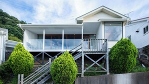 Een modern huis met twee verdiepingen, een balkon, een trap en twee goed onderhouden groene struiken.