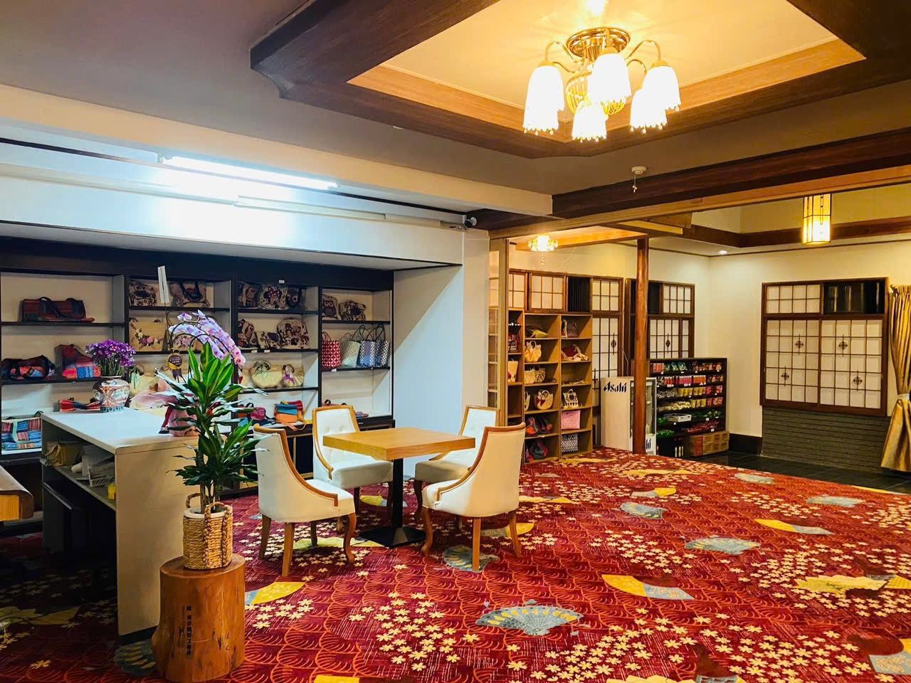 A room with a dining table and chairs, a bookshelf, and a patterned carpet.