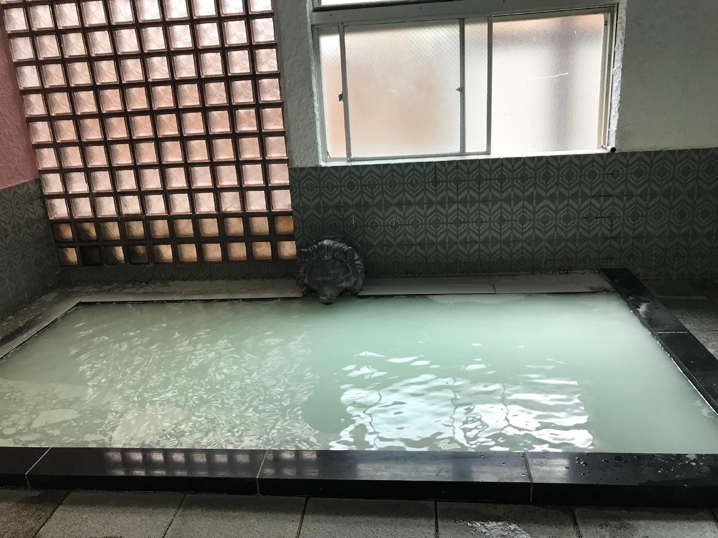 A rectangular hot tub with a tiled floor and a decorative headrest.