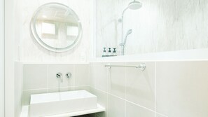 A modern bathroom with a round mirror, a handheld showerhead, and a white sink with two faucets. - Hummer Village (Kamiamakusa)