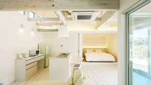 A modern hotel room with a kitchenette, a bed with a headboard, and a large window offering a view. - Hummer Village (Kamiamakusa)