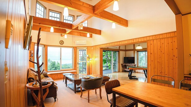 Amplia sala de estar con vigas de madera, ventanas grandes, mesa de billar y televisor.
