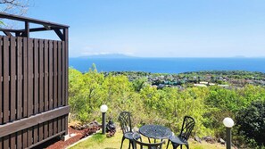 Une terrasse en bois avec une table et des chaises, d’où l’on a vue sur une ville côtière et la mer.