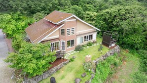 Una casa de dos plantas con techo inclinado, rodeada de abundante vegetación y un sendero de piedra que conduce a la entrada.
