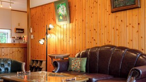 Une pièce aux murs lambrissés, avec un canapé en cuir, une table basse en verre et un luminaire fixé au mur.