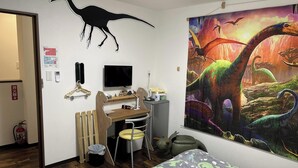 Lastenhuone, jonka seinällä on dinosaurusteemainen seinämaalaus, ja jossa on työpöytä tietokoneineen sekä sänky.