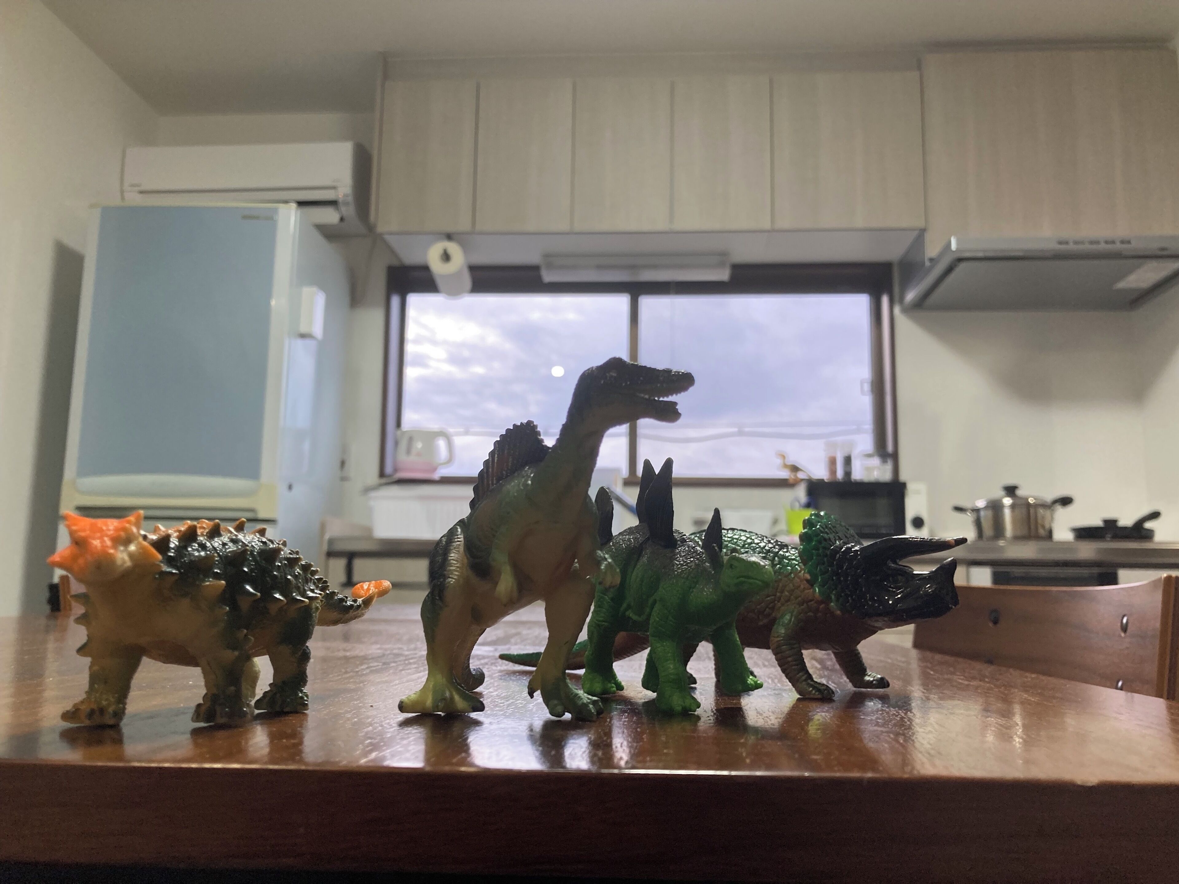 A kitchen with cabinets, a window, and a countertop with dinosaur figurines.
