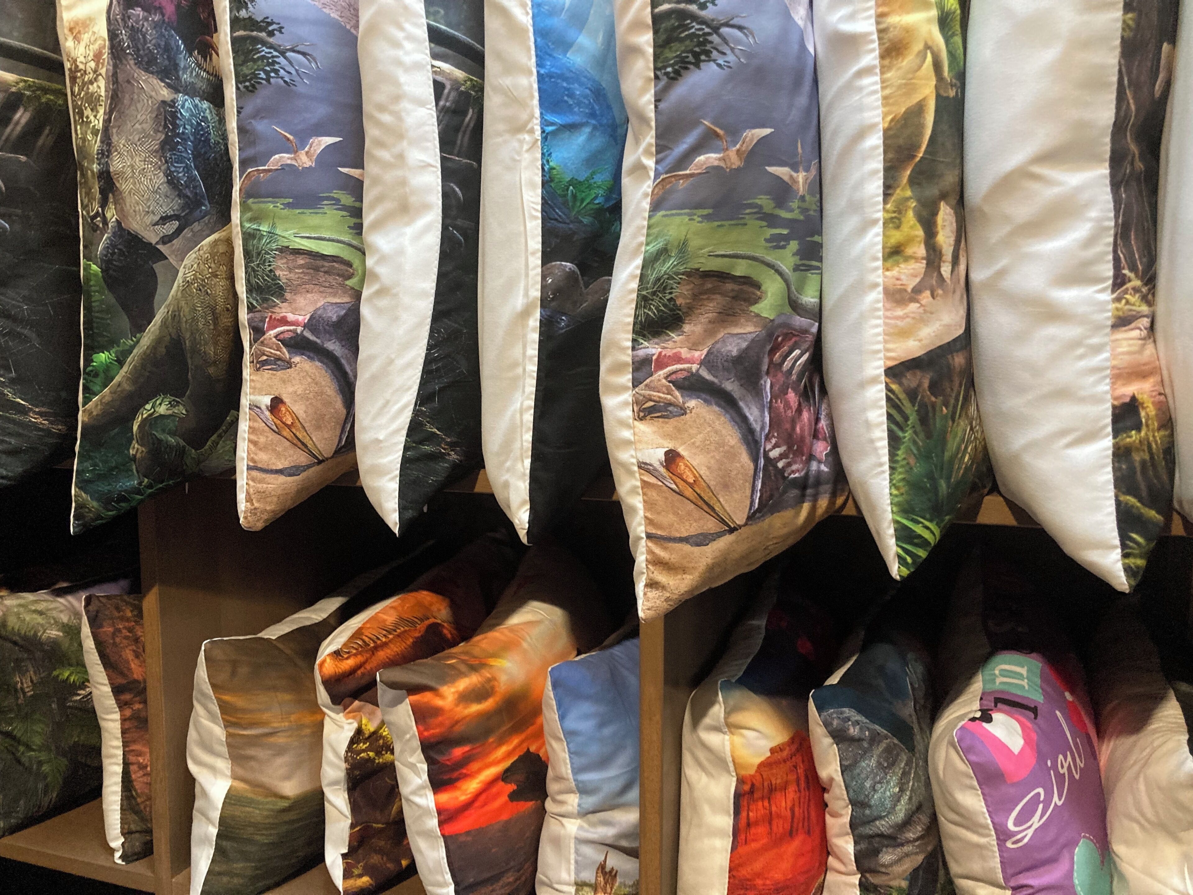 A display of pillows with various designs, including jungle and dinosaur themes.