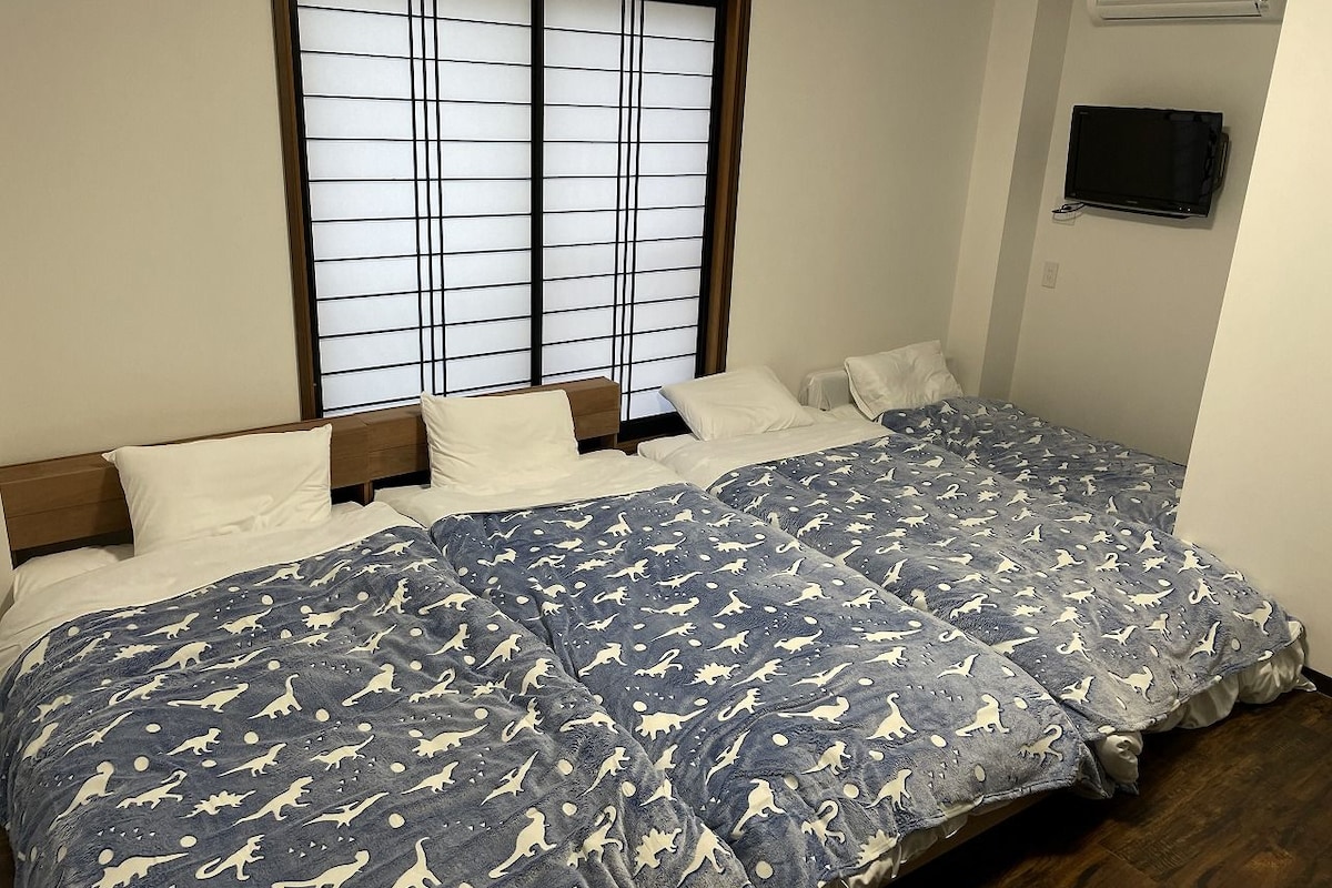 Een slaapkamer met een groot bed, een raam met zonwering, een aan de muur bevestigde televisie en een klein airco-apparaat.