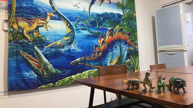 Ruokailutilassa on suuri seinämaalaus, jossa on kuvattuna dinosauruksia, sekä puinen pöytä ja useita dinosaurushahmoja pöydällä.