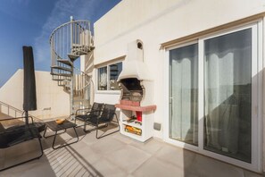 A rooftop terrace with a barbecue grill, two lounge chairs, a spiral staircase, and a sliding glass door. - Gozo Penthouse with Terrace, BBQ & Private Roof (Gozo)