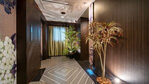 A hallway with a patterned floor, a potted plant, and a wall-mounted security camera. - Noblesse (Kobe)