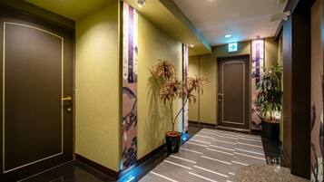 A hotel hallway with doors, a carpeted floor, and potted plants.