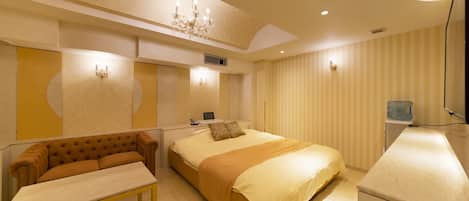A hotel room with a bed, a sofa, a desk, and a water dispenser.