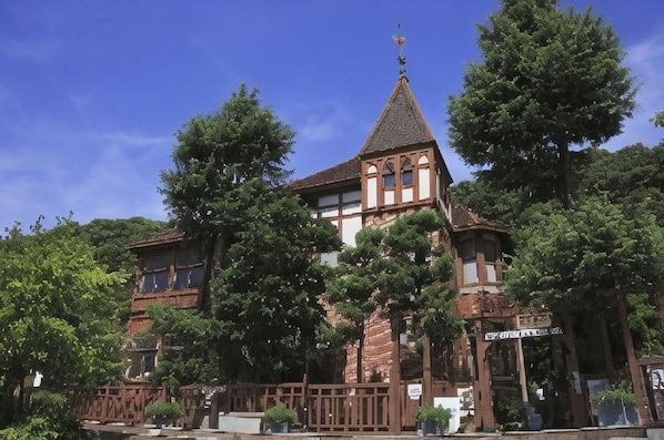 Un edificio histórico con una torre destacada, rodeado de exuberante vegetación.