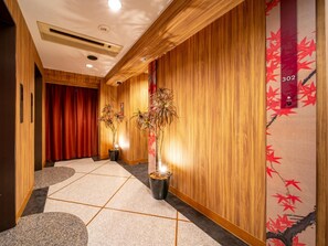 Ein Hotelkorridor mit Holzwandverkleidung, einem roten Vorhang, Topfpflanzen und einem Nummernschild an der Wand.