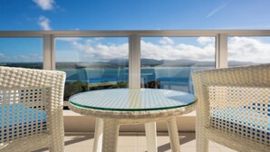 Een balkon met rieten stoelen en een glazen tafel, met uitzicht op een prachtig landschap.