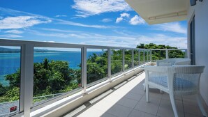 Een balkon met witte rieten meubels, een helder uitzicht op zee en begroeiing, en een betegelde vloer.