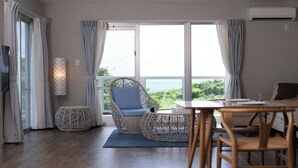 Een kamer met een groot raam, rieten meubels, een tafel en een stoel.