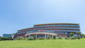 A multi-story hotel with a curved facade, balconies, and a landscaped front lawn. - Lectore Hayama Shonan Kokusai Mura (Hayama)