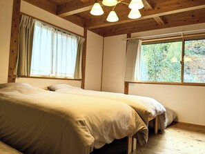 Een kamer met twee bedden, houten balken en grote ramen voorzien van gordijnen.