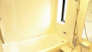 Un baño pequeño y moderno con una bañera blanca, un cabezal de ducha manual y una ventana pequeña.