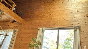 Interior de madera con comedor, una ventana con cortinas y un techo con lámparas colgantes.