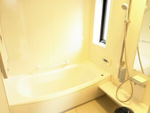Een compacte, moderne badkamer met een witte badkuip, een handdouche en een klein raam.