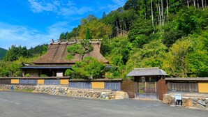 A traditional Japanese building with a thatched roof, surrounded by lush greenery and a stone wall. - Miyama Resort Kayabukitei (Nantan)