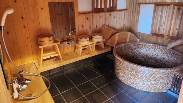 A wooden sauna room with a large stone hot tub, wooden benches, and a sauna heater. - Miyama Resort Kayabukitei (Nantan)