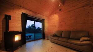 A wooden cabin interior with a sofa, a fireplace, and a large sliding glass door. - Cottage Oyumino (Chiba)