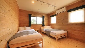 A wooden-paneled room with two beds, a small table, and an air conditioning unit. - Cottage Oyumino (Chiba)